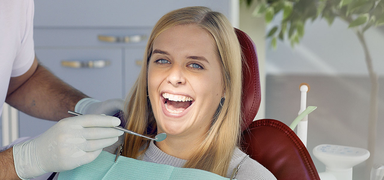 Eine Frau auf dem Zahnarztstuhl öffnet den Mund ganz weit für die Untersuchung. 