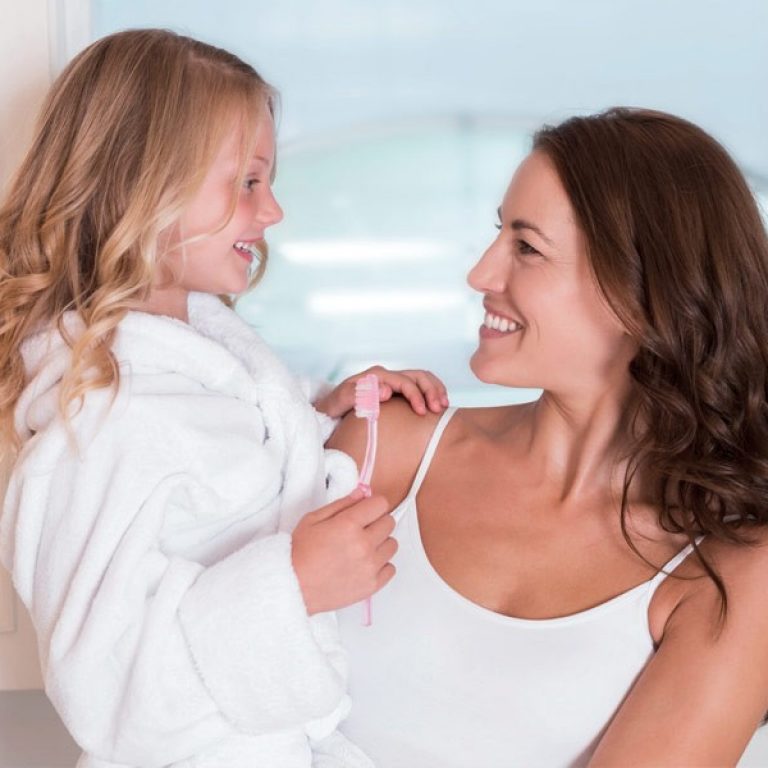 Eine Frau hält ihre Tochter auf dem Arm. Diese lächelt, eine Zahnbürste in der Hand.